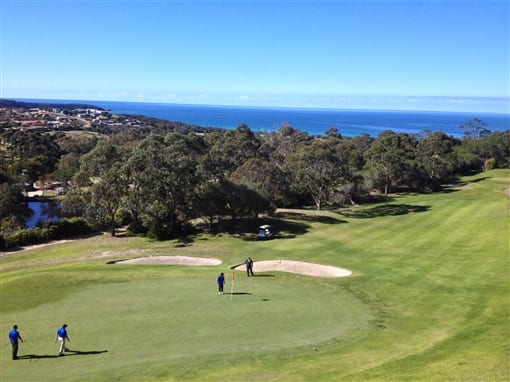 A golf course on a sunny day, its fairway running down to the trees